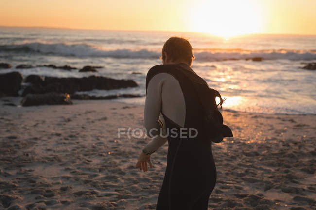 Surfboard removing wet suit at beach during sunset — Stock Photo