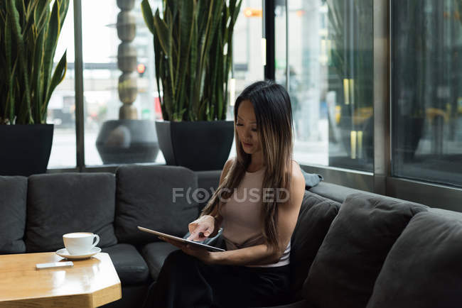 Empresária sentada no sofá trabalhando em seu tablet na cafetaria — Fotografia de Stock