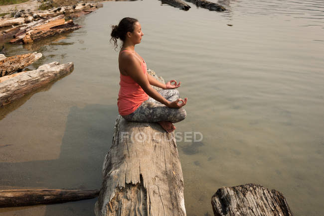 Donna in forma seduta a meditare postura su un tronco d'albero caduto in una giornata di sole — Foto stock