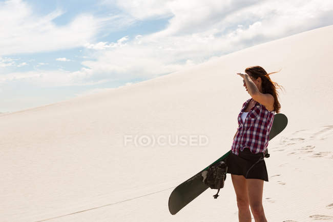 Mulher com sandboard em pé no deserto em um dia ensolarado — Fotografia de Stock