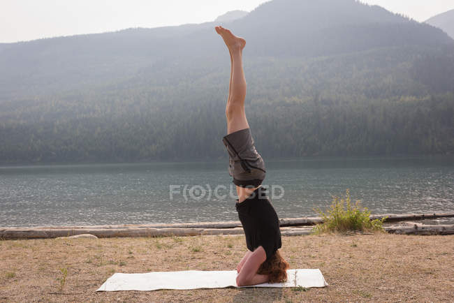 Side view of sporty man practicing head stand near the sea coast — Stock Photo
