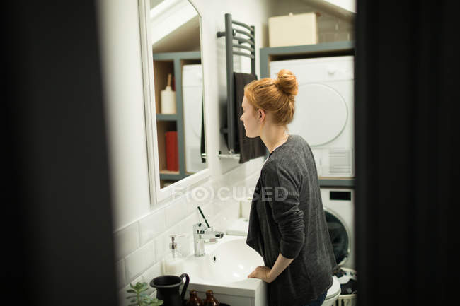 Молодая женщина смотрит в зеркало ванной дома — стоковое фото