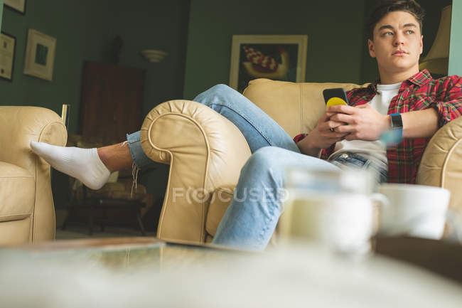 Человек с помощью мобильного телефона во время отдыха в кресле в гостиной на дому . — стоковое фото