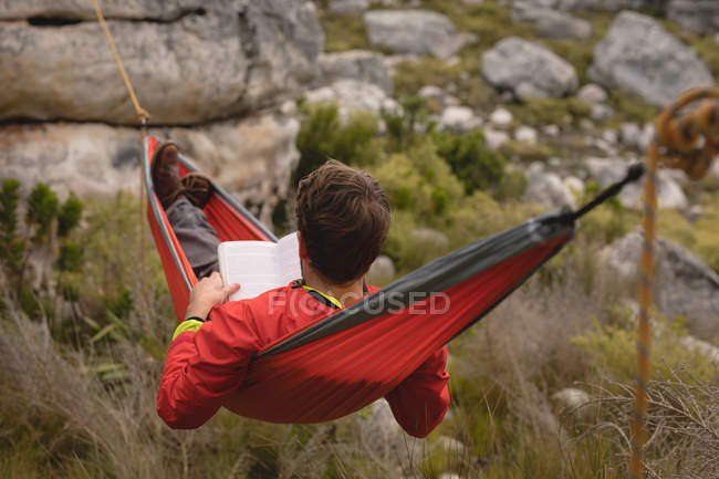 Hiker lying in hammock reading novel on a sunny day — Stock Photo