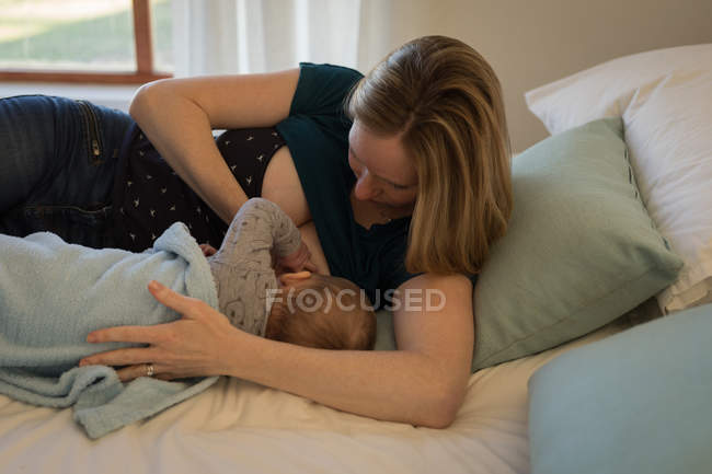 Mãe segurando e amamentando bebê na cama em casa . — Fotografia de Stock