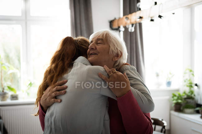 Emocional avó e neta abraçando uns aos outros na sala de estar — Fotografia de Stock
