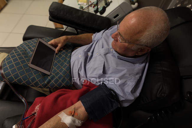 Hombre mayor usando tableta digital mientras dona sangre en banco de sangre - foto de stock