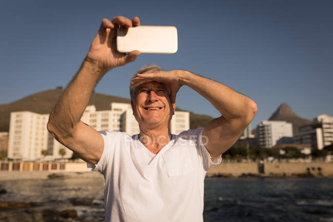 Щасливий старший чоловік бере селфі біля моря — стокове фото