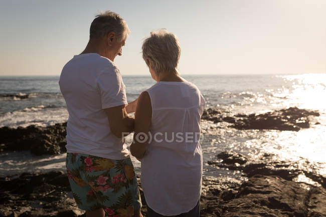Вид спереду на старшу пару, що стоїть біля моря на сонячний день — стокове фото