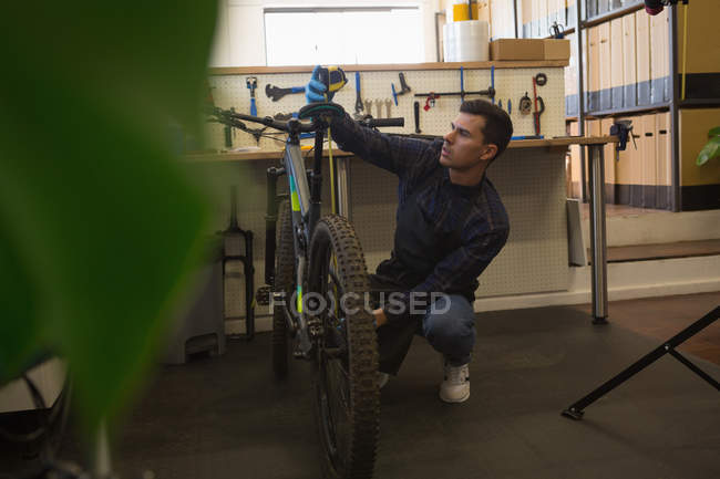 Молодой человек измеряет длину велосипедного сиденья в мастерской — стоковое фото