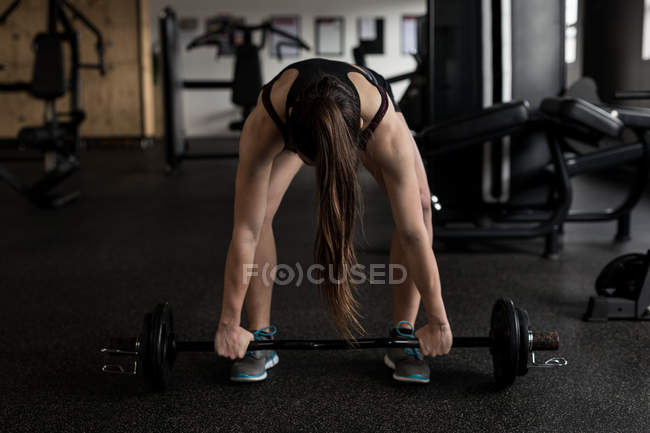 Fit woman lifting barbell in fitness studio — Stock Photo