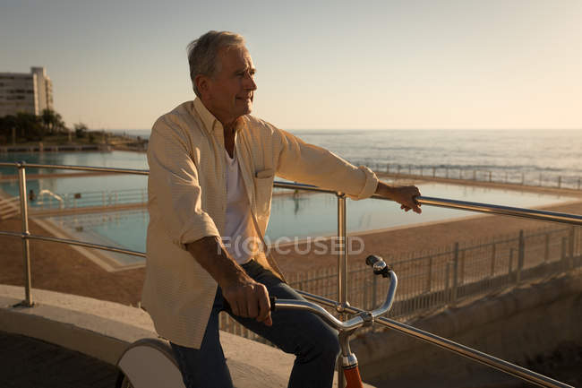 Задумчивый пожилой человек, сидящий на велосипеде на набережной — стоковое фото