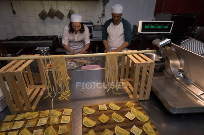 Panadero masculino y femenino preparando pasta en panadería - foto de stock