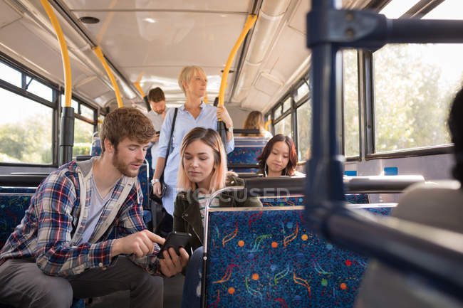 Jeune couple utilisant un téléphone portable tout en voyageant en bus moderne — Photo de stock