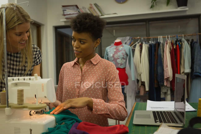 Diseñadores de moda interactuando mientras utilizan la máquina de coser en el estudio de moda - foto de stock