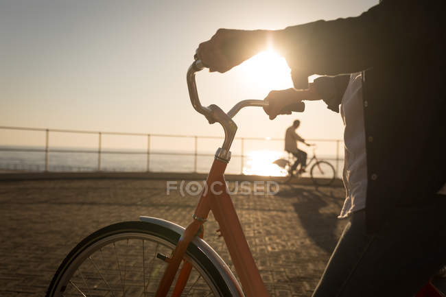 Sección media de la mujer mayor sosteniendo la bicicleta en el paseo marítimo - foto de stock