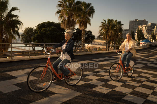 Casal sênior andar de bicicleta no passeio em um dia ensolarado — Fotografia de Stock