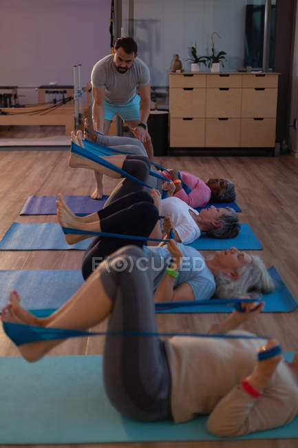 Treinador auxiliando mulheres idosas na realização de ioga no centro de ioga — Fotografia de Stock