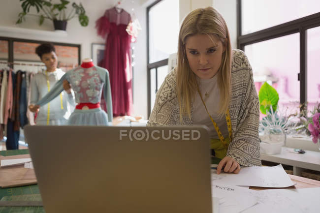 Hermoso diseñador de moda utilizando el ordenador portátil en estudio de moda - foto de stock