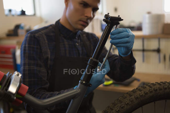 Hombre atento reparación de asiento de bicicleta en el taller - foto de stock