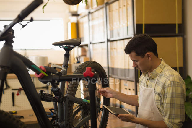 Uomo che utilizza tablet digitale mentre ripara la bicicletta in officina — Foto stock