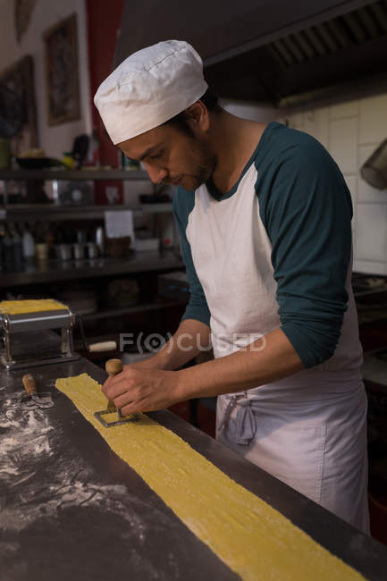 Padeiro macho macarrão de corte na padaria — Fotografia de Stock