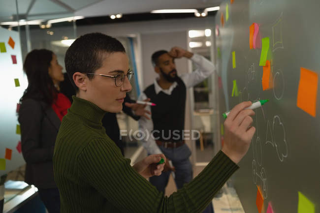 Businesswoman writing on glass board at office — Stock Photo