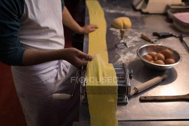 Primer plano del panadero utilizando la máquina para preparar pasta en la panadería - foto de stock