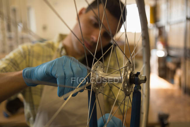 Close-up of man talking on mobile phone while repairing bicycle wheel in workshop — Stock Photo
