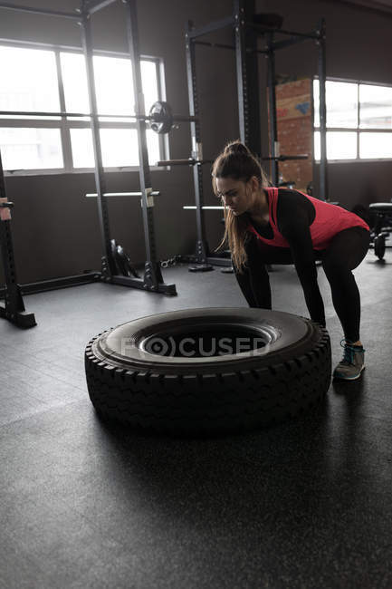 Fit woman exercising with tyre in fitness studio — Stock Photo