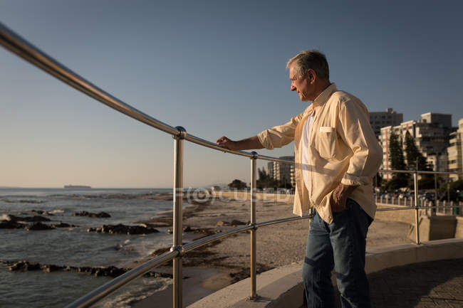 Homme âgé debout près de la mer à la promenade par une journée ensoleillée — Photo de stock
