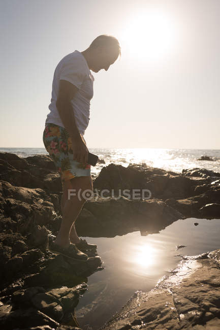 Vista laterale dell'uomo anziano in piedi sulla roccia vicino al mare nella giornata di sole — Foto stock