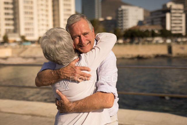 Улыбающаяся старшая пара обнимает друг друга на прогулке — стоковое фото