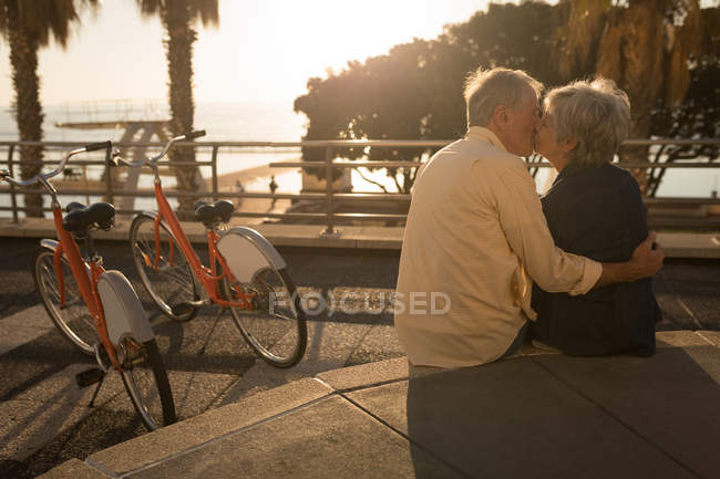 Старшая пара целуется на стене сиденья на прогулке в солнечный день — стоковое фото