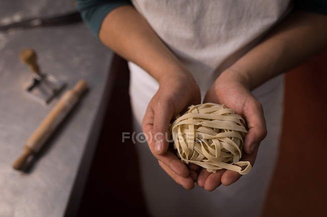 Baker holding tagliatelle in a hand in a bakery — Stock Photo