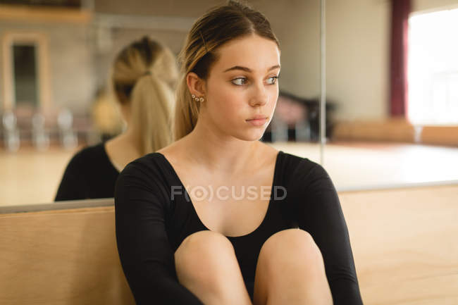 Молода балерина сидить на підлозі в танцювальній студії — стокове фото