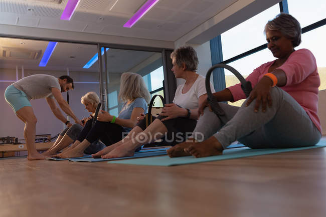 Treinador auxiliando mulheres idosas na realização de ioga no centro de ioga — Fotografia de Stock