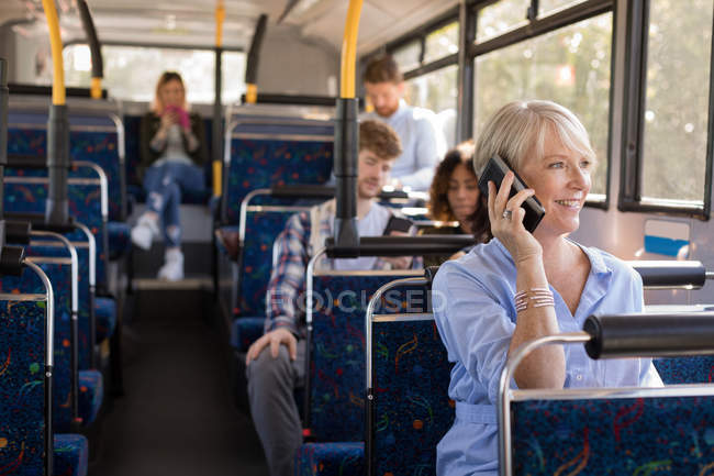 Пригородная женщина разговаривает по мобильному телефону во время путешествия в современном автобусе — стоковое фото