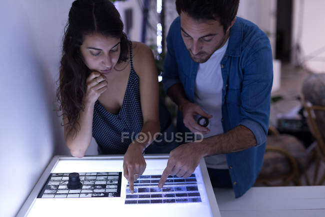 Male photographer and female model discussing over negative filmstrip in photo studio — Stock Photo