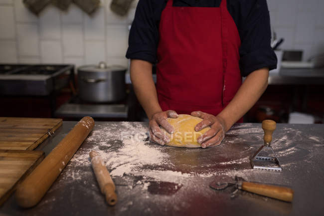 Panadero sosteniendo una masa de prueba en la panadería - foto de stock