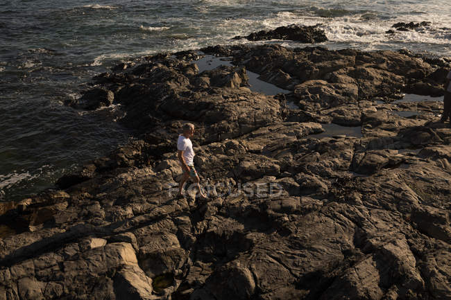 Homme âgé marchant sur le rocher à la plage par une journée ensoleillée — Photo de stock