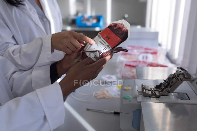 Técnicos de laboratorio discutiendo sobre bolsa de sangre en banco de sangre - foto de stock
