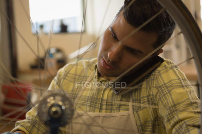 Крупним планом чоловік розмовляє по мобільному телефону під час ремонту велосипеда в майстерні — стокове фото