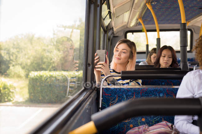 Female commuter taking selfie on mobile phone while travelling in modern bus — Stock Photo