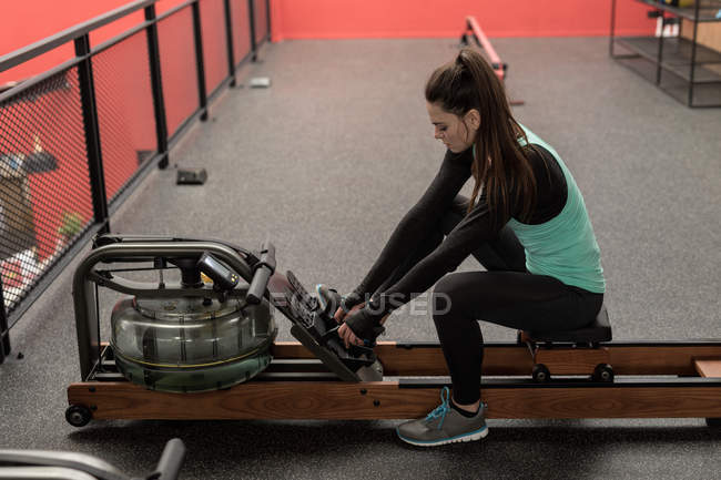 Young woman using rowing machine in fitness studio — Stock Photo