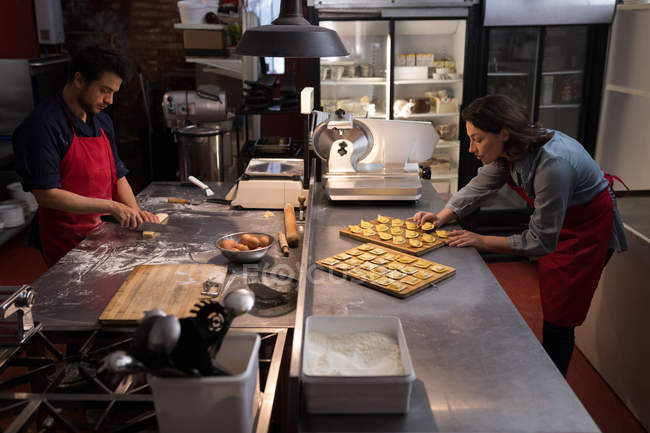 Женщина-пекарь с другими делает макароны в пекарне — стоковое фото