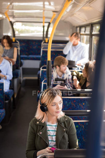 Comutador feminino ouvindo música enquanto viaja em ônibus moderno — Fotografia de Stock