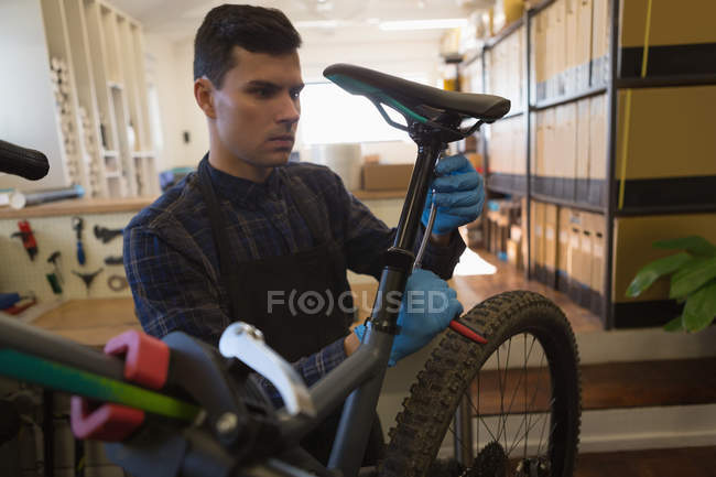 Homem ajustando assento de bicicleta com chave na oficina — Fotografia de Stock