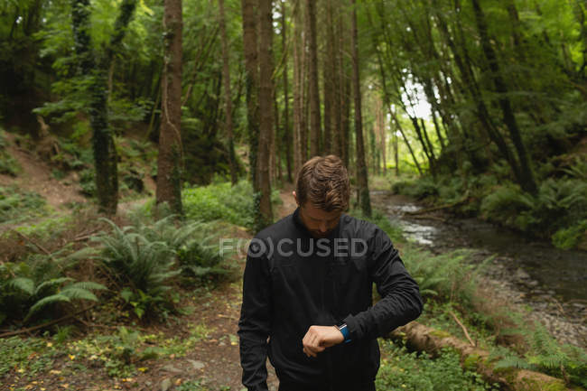 Jovem olhando relógio inteligente na floresta — Fotografia de Stock