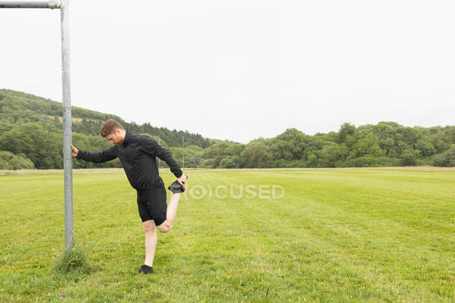 Молодий чоловік розтягується на зеленому пейзажі — стокове фото